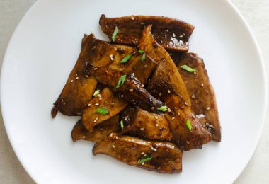 Beyaz tabakta susamlı ve yeşil soğanlı eryngii mantarı. Gochujang Kral İstiridye Mantarı pişirme süreci. Geleneksel Kore mutfağı kavramı. Vejetaryen ve yemek. en üstteki görünüm