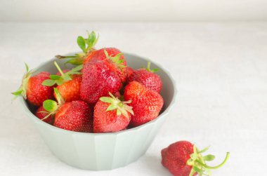 Gri bir masada yeşil bir kasede olgun kırmızı çilekler. Yaz yemeği kavramı. Yatay oryantasyon. Seçici odaklanma. Boşluğu kopyala