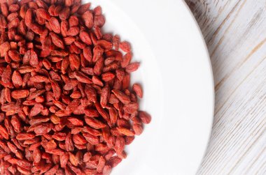 Ahşap bir masada beyaz bir tabağa serpiştirilmiş kırmızı kurt üzümü. Süper yiyecek konsepti. Vejetaryen ve vejetaryen yemekleri. Yatay oryantasyon. Üst görünüm.