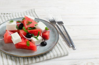 Karpuzlu yaz salatası, beyaz ahşap bir masada iki çatallı gri bir tabakta beyaz peynir, zeytin ve nane. Vejetaryen yemeği kavramı. Uzayı kopyala Yatay yönelim.