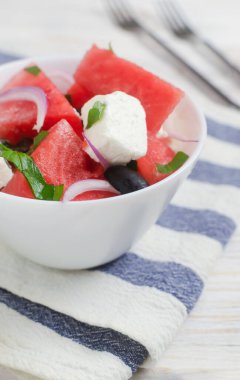 Karpuzlu yaz salatası, peynirli feta, zeytin ve çizgili peçetede beyaz bir kasede nane. Sağlıklı beslenme kavramı. Vejetaryen, vejetaryen. Dikey oryantasyon. Seçici odak.