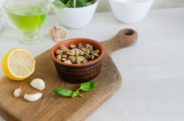 Tahta bir tahtanın üzerinde, fesleğen, limon ve sarımsaklı seramik bir kasede soyulmuş şam fıstığı. Fıstıklı pesto yapma süreci. Yatay oryantasyon. Seçici odaklanma. Boşluğu kopyala