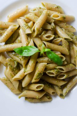 Masanın üzerinde fesleğen filizi ve şam fıstıklı makarna. İtalyan mutfağı konsepti. Dikey oryantasyon. Seçici odaklanma. Üst görünüm