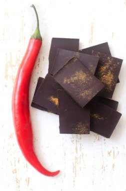 Masadaki beyaz tahta kesme tahtasının üzerinde kırmızı biberli ekstra koyu çikolata parçaları. Trend gıda konsepti. Seçici odaklanma. Dikey oryantasyon. Üst görünüm