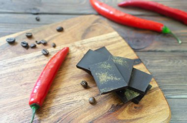 Masadaki tahta kesme tahtasının üzerinde üç kırmızı biberli ekstra koyu çikolata parçaları. Trend gıda konsepti. Seçici odaklanma. Yatay yönelim.