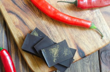 Masadaki tahta kesme tahtasının üzerinde üç kırmızı biberli ekstra koyu çikolata parçaları. Trend gıda konsepti. Seçici odaklanma. Yatay oryantasyon. Üst görünüm.