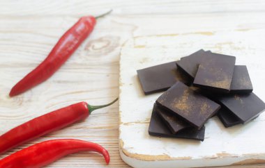 Ekstra koyu çikolata parçaları ve masada beyaz ahşap bir tahta üzerinde üç kırmızı biber. Trend gıda konsepti. Seçici odaklanma. Yatay yönelim.