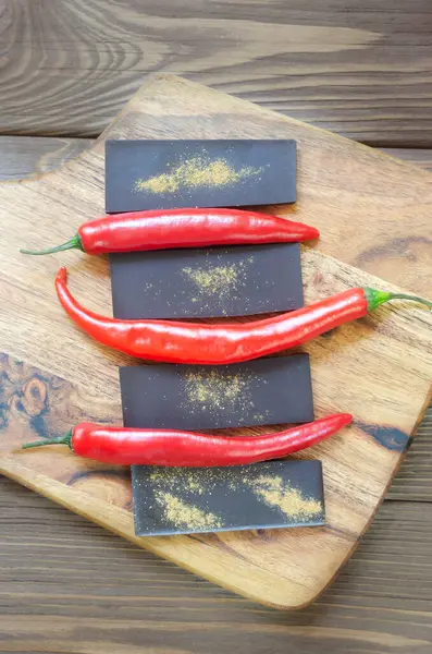 Masadaki tahta kesme tahtasının üzerinde üç kırmızı biberli ekstra koyu çikolata. Trend gıda konsepti. Seçici odaklanma. Dikey oryantasyon. Üst görünüm