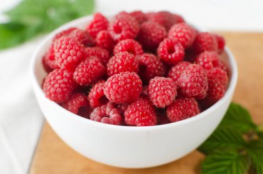 Beyaz arka planda yeşil yapraklı bir kasede olgun pembe ahududular. Yaz çileği hasadı kavramı. Yatay oryantasyon. Seçici odak.