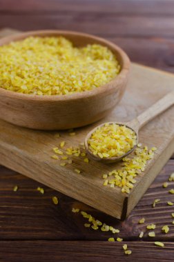 Tahta bir kasede çiğ bulgur taneleri ve kahverengi bir masada kesme tahtasının üzerinde bir kaşık. Sağlıklı beslenme konsepti. Vejetaryen ve vejetaryen yemekleri. Diyet olsun. Kırsal tarzda. Dikey yönelim.