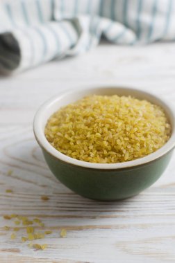 Beyaz ahşap bir masada seramik yeşil bir kasede çiğ bulgur taneleri. Sağlıklı beslenme konsepti. Vejetaryen ve vejetaryen yemekleri. Diyet olsun. Kırsal tarzda. Dikey yönelim.