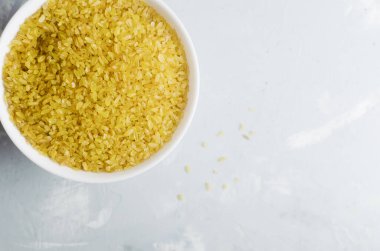Gri arka planda seramik beyaz bir kasede çiğ bulgur taneleri. Sağlıklı beslenme konsepti. Vejetaryen ve vejetaryen yemekleri. Kırsal tarzda. Yatay oryantasyon. Uzayı kopyala Üst görünüm