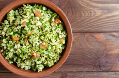Oryantal salata Tabbouleh 'i ahşap bir masada seramik bir kasede. Geleneksel Lübnan mutfağı veya Suriye mutfağı kavramı. Vejetaryen ya da vejetaryen yemeği. Seçici odaklanma. Yatay oryantasyon. Üst Manzara. Boşluğu kopyala
