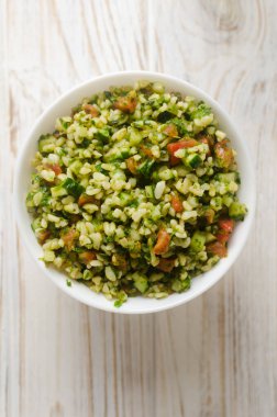 Doğu salatası Tabbouleh, ahşap bir masada beyaz bir kase içinde. Geleneksel Lübnan mutfağı veya Suriye mutfağı kavramı. Vejetaryen ya da vejetaryen yemeği. Seçici odaklanma. Dikey oryantasyon. Üst görünüm.