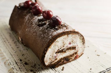 Black Forest roll cake with chocolate and cherries on a white plate. Homemade delicious pastries with delicate cream. Retro recipe concept. Horizontal orientation. Selective focus. Copy space.