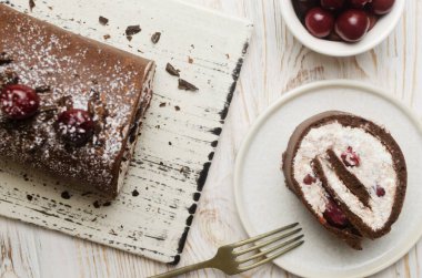 Black Forest roll cake with chocolate and cherries on a white plate. Homemade delicious pastries with delicate cream. Retro recipe concept. Horizontal orientation. Selective focus. Top view