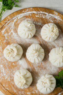 Maydanozlu çiğ khinkali. Masasında un olan yuvarlak bir kesim tahtası. Geleneksel Gürcü mutfağı kavramı. Dikey oryantasyon. Seçici odaklanma. Üst görünüm