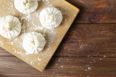 Tahta üzerinde un olan bir kesme tahtasının üzerinde çiğ hinkali. Geleneksel Gürcü mutfağı kavramı. Kırsal tarzda. Yatay oryantasyon. Seçici odaklanma. Üst Manzara. Boşluğu kopyala