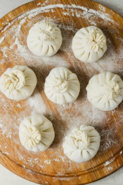 Yuvarlak bir kesim tahtasında çiğ hinkali ve masada un. Geleneksel Gürcü mutfağı kavramı. Dikey oryantasyon. Seçici odaklanma. Üst görünüm