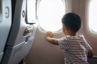 Asyalı çocuklar uçak koltuğunda otururken gökyüzünün ve uçak penceresinin dışındaki bulutların görüntüsüne bakarlar..