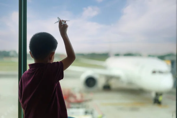 亚洲男孩的飞机模型在空荡荡的机场候机楼等待起飞 向窗外望去 穿着T恤和短裤的孩子站在休息室等飞机 家庭旅行概念 — 图库照片