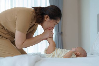 Asyalı anne yeni doğmuş bebeğiyle evdeki yatak odasında oynuyor. Aile ilişkilerini ilerletmek ve bebeğin gelişimi için.