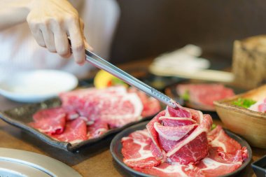 Kadın eli, wagyu bifteğini tabağa koymak için maşa kullanıyor, kömürün üzerinde ızgara yapmaya hazır, bir Japon restoranında yemek deneyimini arttırıyor.