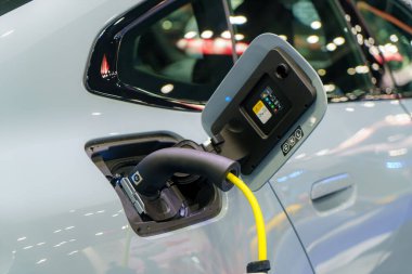 EV otomobili şarj istasyonunda dinleniyor, elektrik kablosu bağlı, şehir ulaşımının çevre dostu geleceğini somutlaştırıyor.