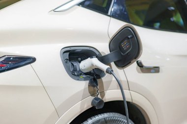 EV otomobili şarj istasyonunda dinleniyor, elektrik kablosu bağlı, şehir ulaşımının çevre dostu geleceğini somutlaştırıyor.
