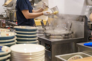 Ramen restoranının coşkulu mutfağı ustalıkla işlenmiş eriştelere çorba buharı yapıyor, bu sahne aşçılık ustalığını ve özgün tatlara olan bağlılığını somutlaştırıyor.