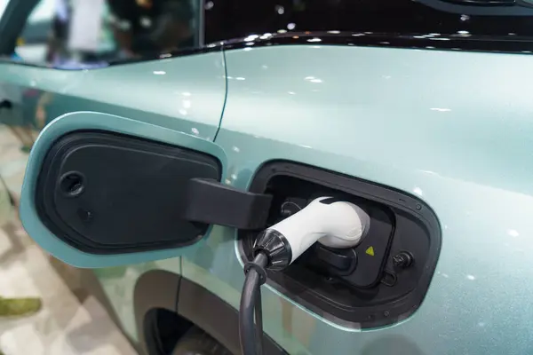 EV car at rest, connected to a charging station, embodying the sustainable future of urban transportation. The power cable seamlessly links the vehicle to clean energy, symbolizing a harmonious blend of technology and environmental consciousness.