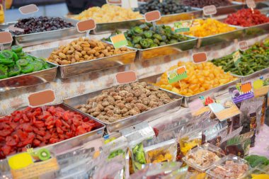 Markette metal tepsilerde sunulan canlı ve renkli meyve ve fındık çeşitliliği ve sağlıklı çerez seçeneklerinin cazibesini vurguluyor..