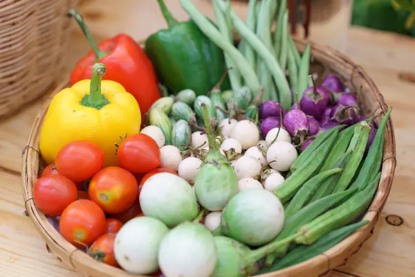 トマト ベルペッパー ナッツ オクラを含む新鮮な野菜の鮮やかな選択は 素朴なウィッカーバスケットで 有機農産物を展示しています ストックフォト