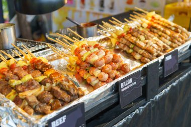 Tavuk, domuz eti ve domuz pastırmasına sarılı sosislerle birlikte bir sokak yemeği standında sergilenen iştah açıcı bir dizi şiş.