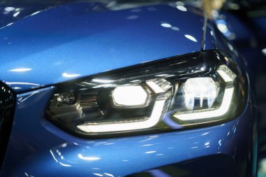 Gece aydınlanması sırasında arabanın farlarını yakından çek. Gösterişli tasarım ve güçlü kirişler önlerindeki yolda berraklık ve görüş sağlayarak güvenlik ve entelektüelliği simgeliyor.