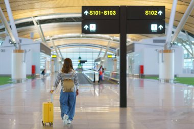 Geniş, modern bir havaalanı terminalinde yürüyen Asyalı kadının arka görüntüsü.