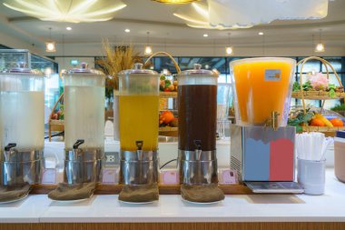 Kahvaltı büfesinde bir sıra içecek dağıtıcısı. Kurulum, her biri farklı tipte içeceklerle dolu dört büyük dağıtıcıyı içeriyor.