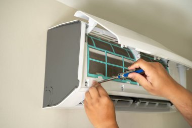 Erkek profesyonel teknisyen içeride klimayı tamir eden bir elektrikçiyi tamir ediyor. Hava filtresi kaldırılıyor. Sıcaklık onarılıyor.