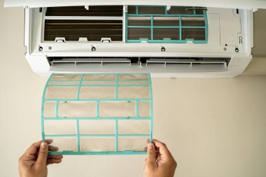 Erkek profesyonel teknisyen içeride klimayı tamir eden bir elektrikçiyi tamir ediyor. Hava filtresi kaldırılıyor. Sıcaklık onarılıyor.