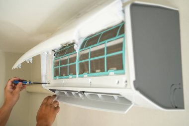 Erkek profesyonel teknisyen içeride klimayı tamir eden bir elektrikçiyi tamir ediyor. Hava filtresi kaldırılıyor. Sıcaklık onarılıyor.