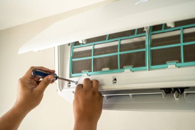 Erkek profesyonel teknisyen içeride klimayı tamir eden bir elektrikçiyi tamir ediyor. Hava filtresi kaldırılıyor. Sıcaklık onarılıyor.