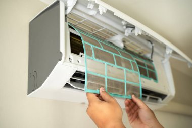 Erkek profesyonel teknisyen içeride klimayı tamir eden bir elektrikçiyi tamir ediyor. Hava filtresi kaldırılıyor. Sıcaklık onarılıyor.