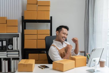 Genç Asyalı mutlu, gülümseyen küçük işletmeler. Birçok insan ürünler sipariş ediyor ve onun iş başarısını evde kutluyor. Tedarik zinciri ve depoda..