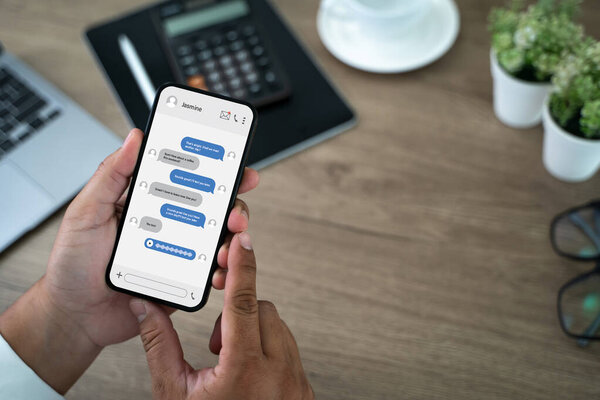 Man chatting on mobile phone chat message online screen app in smartphone on a table with a laptop and a cup