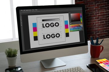 Grafik tasarımcısı bir şirket için Illustrator 'da renk paleti içeren bir marka logosu oluşturmak için tablet ve bilgisayar kullanıyor.