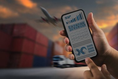 Detaylı grafik ve çizelgeleri gösteren, lojistik ve tedarik zinciri analizini sembolize eden bir akıllı telefonu tutan bir el. Arkaplanda küresel taşımayı temsil eden konteynırlar, bir kamyon ve bir uçak yer alıyor.