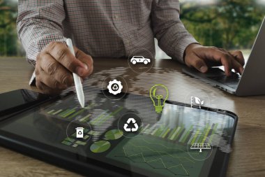 Sürdürülebilir bir iş uygulaması çalışanı, sürdürülebilirlik ve teknoloji ile ilgili dijital simgelerle tablet üzerinde çalışarak, odak çevre dostu