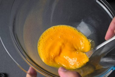 Yumurta çırpıyorum. Bir adamın eli çatallı, cam bir kasede yumurta çırpıyor.
