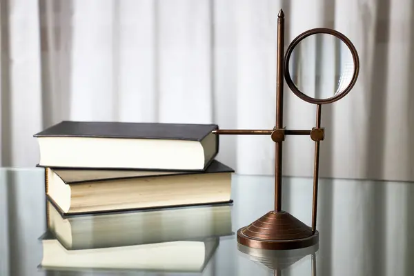 Büyüteç ve kitaplar. Cam bir yüzey ve eski kitaplar üzerinde dönen eski bir büyüteç.