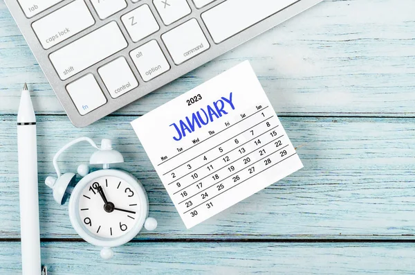 stock image January 2023 Monthly calendar year and alarm clock with keyboard computer on blue wooden background.